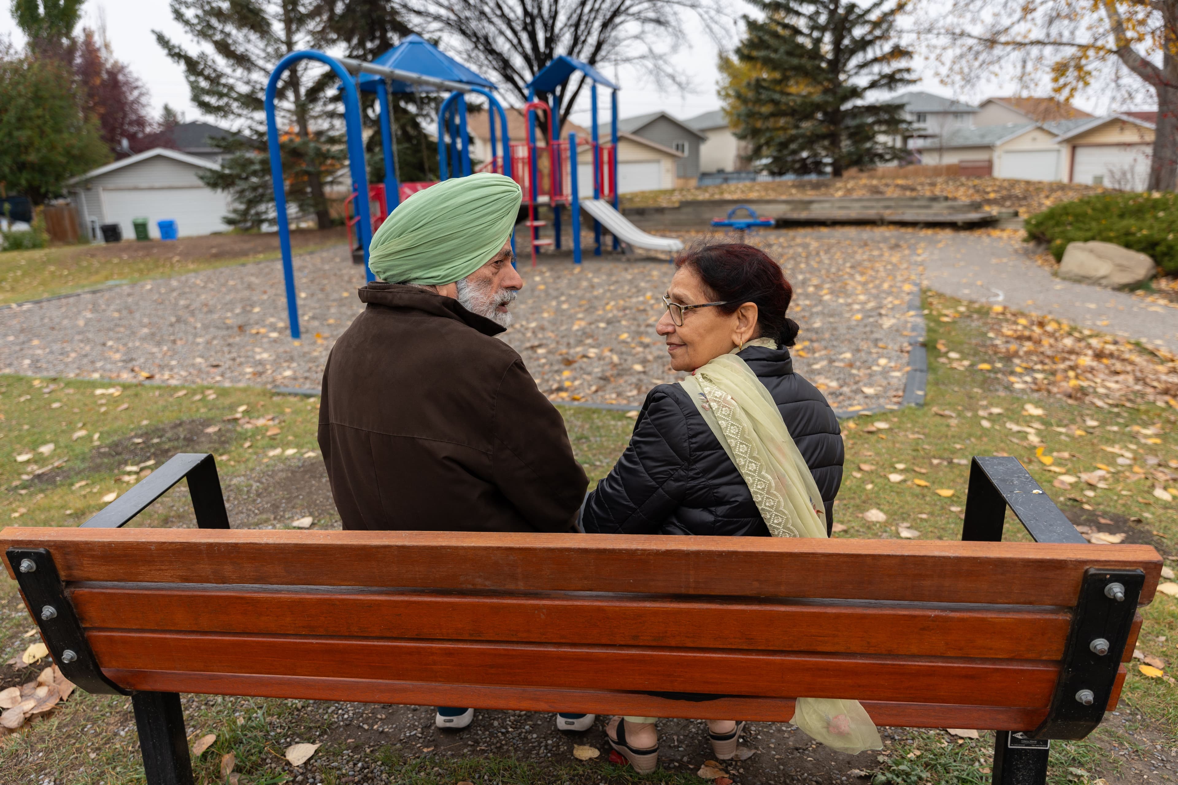 An elderly Sikh couple sitting together on a park bench, talking and smiling