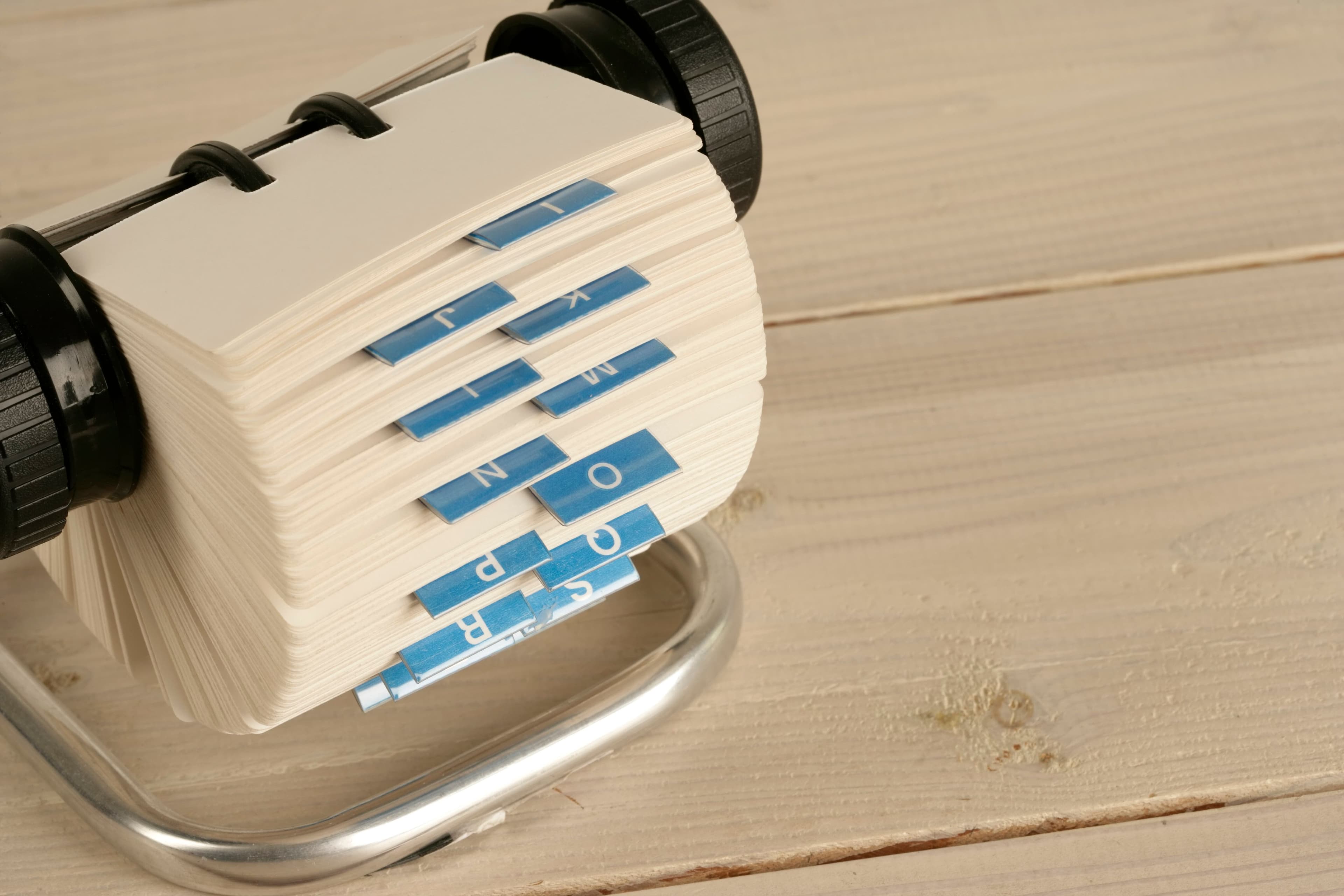 A rotary address file on a wooden desk, alphabet tabs fanned open
