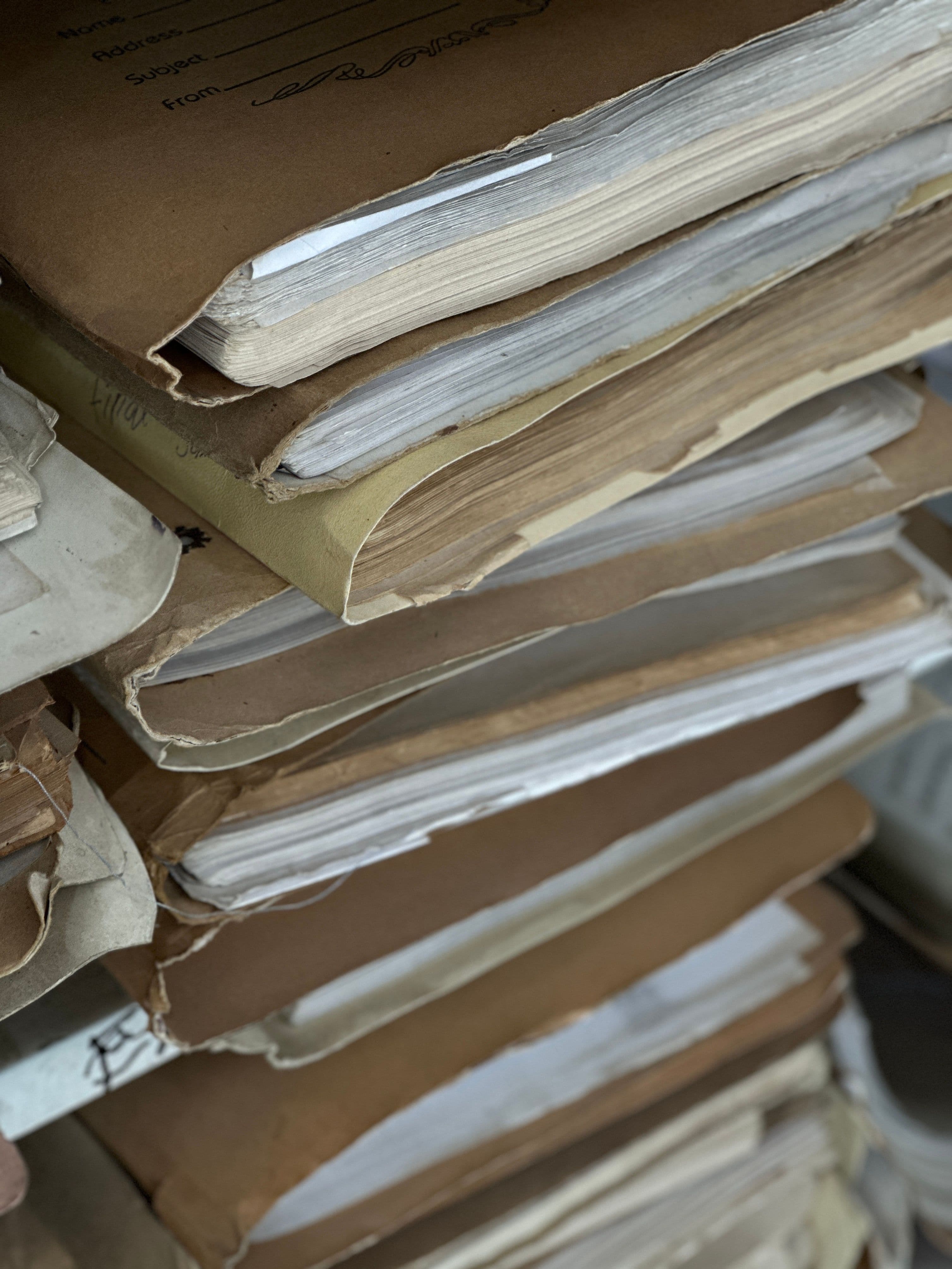 A stack of worn paper folders and files on a shelf